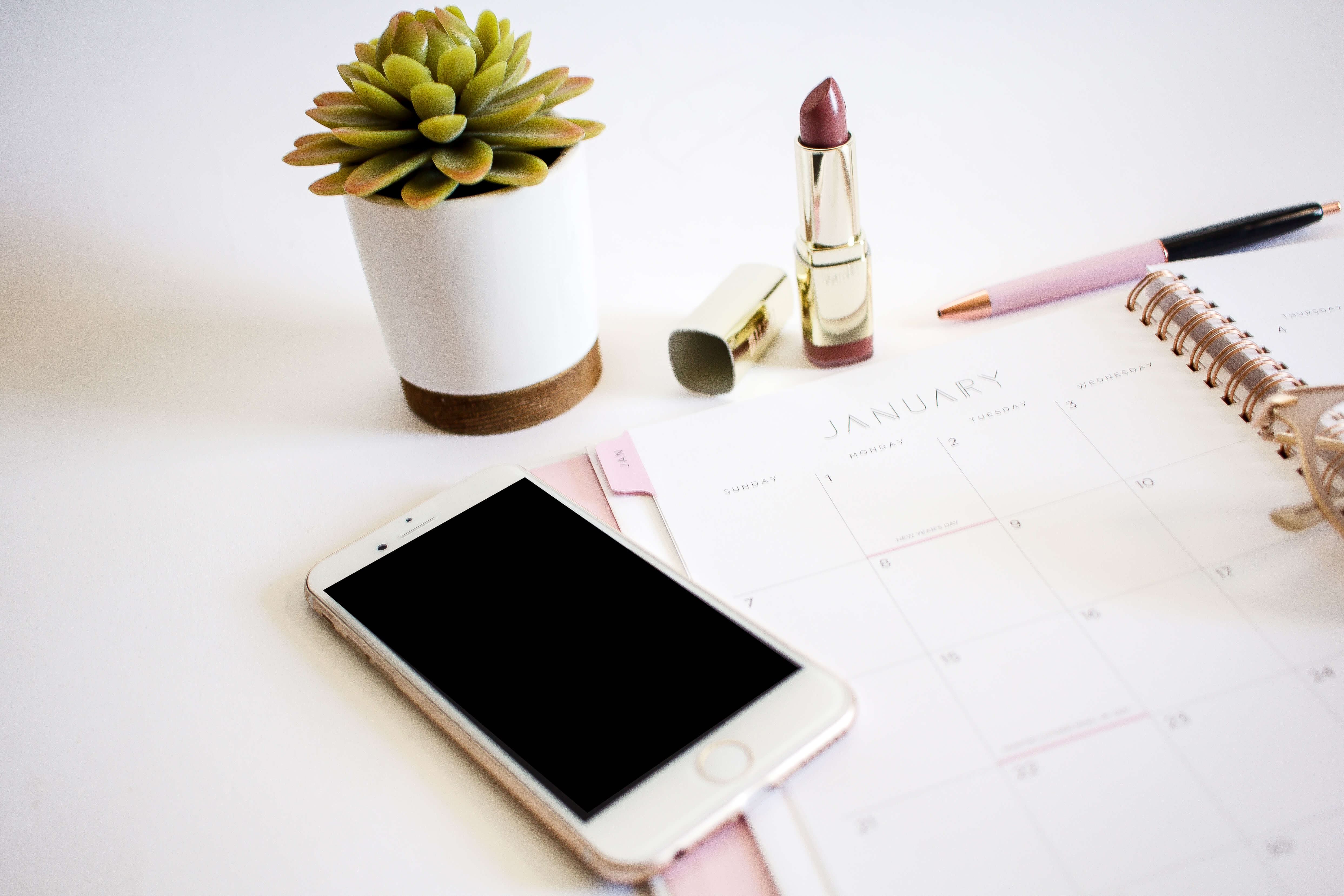 flat lay photo with cell phone, lipstick, calendar and plant