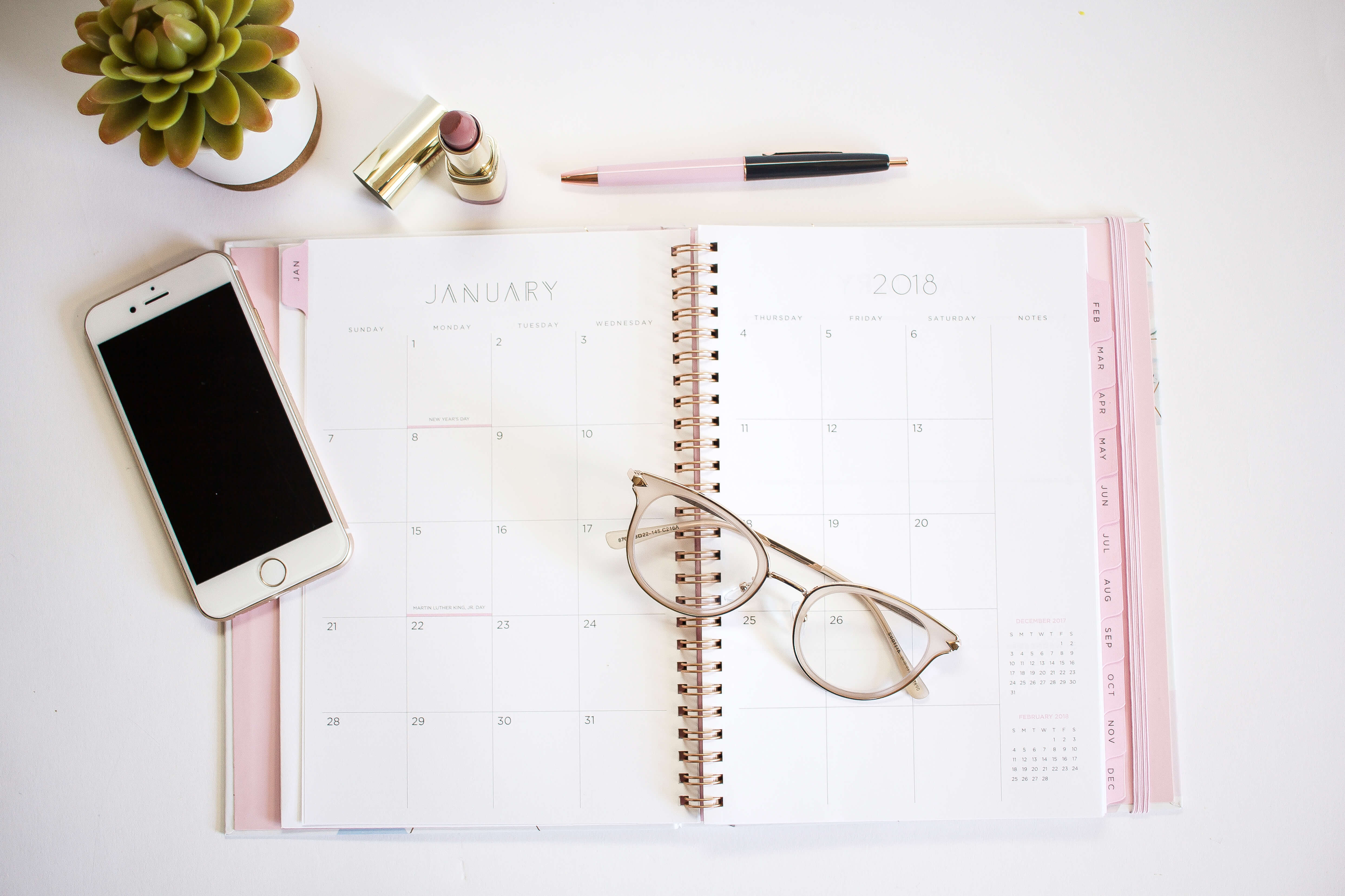 flatlay photo with calendar, cell phone, glass and pen